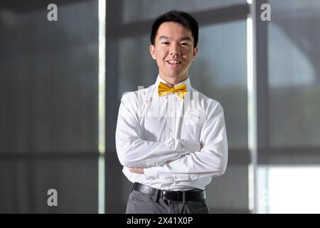 A young man is standing with his arms crossed, posing for the camera at an event. He is a guest speaker at an event with a name tag displaying the nam Stock Photo