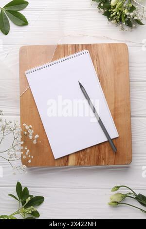 Guest list. Notebook, pencil, beautiful flowers and ribbon on white wooden background, flat lay Stock Photo