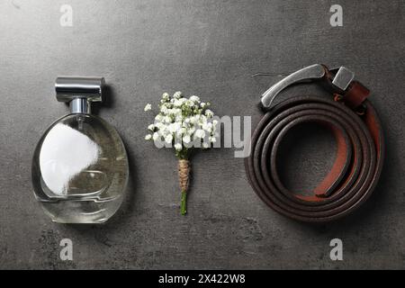 Wedding stuff. Stylish boutonniere, belt and perfume on black table, flat lay Stock Photo