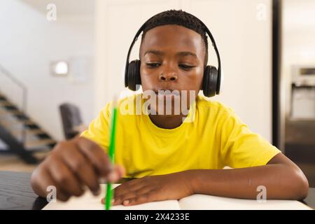 An African American boy wearing headphones, writing in notebook at home Stock Photo