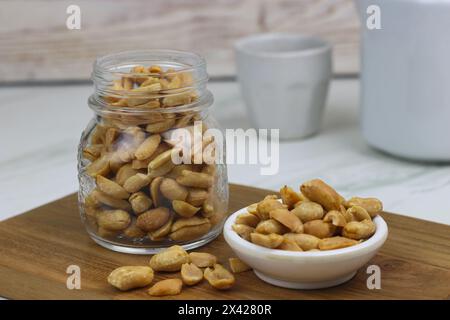 Kacang goreng or fried peanuts in a jar and white plate. Indonesian snack with marble white background, selective focus. Stock Photo