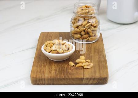 Kacang goreng or fried peanuts in a jar and white plate. Indonesian snack with marble white background, selective focus. Stock Photo