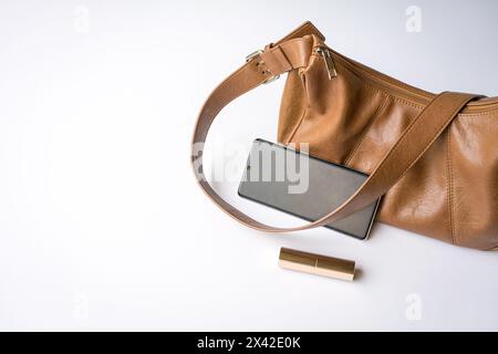 Woman leather handbag with phone and lipstick. On white background, copy space. Stock Photo