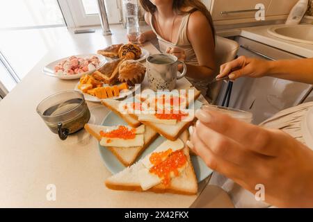 A woman is cutting bread and putting jelly on it. The table is set with a variety of food items, including sandwiches, fruit, and a jar of jelly. The Stock Photo