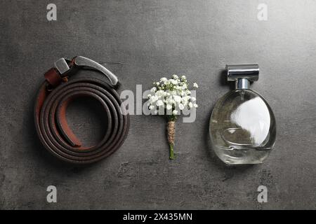 Wedding stuff. Stylish boutonniere, belt and perfume on black table, flat lay Stock Photo