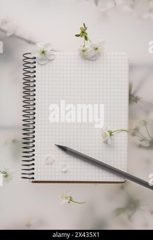 Guest list. Notebook, pencil and beautiful cherry tree blossoms on spring floral background, flat lay Stock Photo