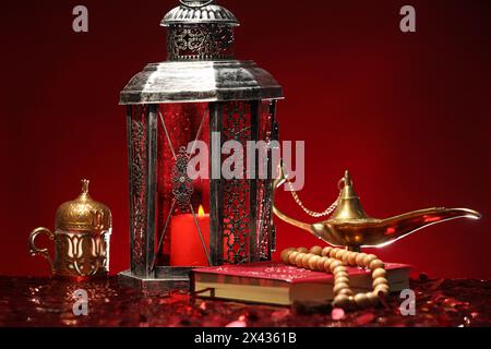 Arabic lantern, Quran, misbaha and Aladdin magic lamp on shiny red table Stock Photo