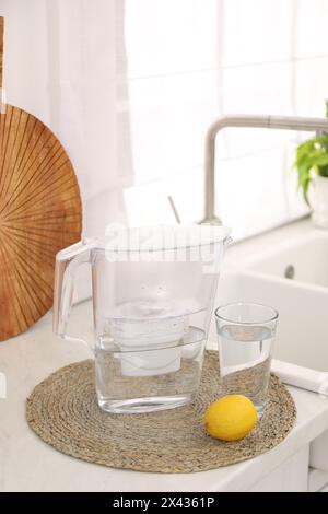 Water filter jug, glass and lemon on countertop in kitchen Stock Photo