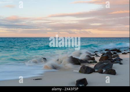 Indian Ocean surf crashing on to rocks on a tropical beach at sunset. Anse Bambous Beach, Fregate Island, Seychelles. Stock Photo
