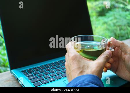 Man holding a cup of tea while working on his laptop Stock Photo