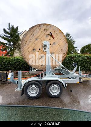 Giant wooden reel of optic fiber cable on a trailer at an installation site, with urban surroundings - internet deployment in the city Stock Photo