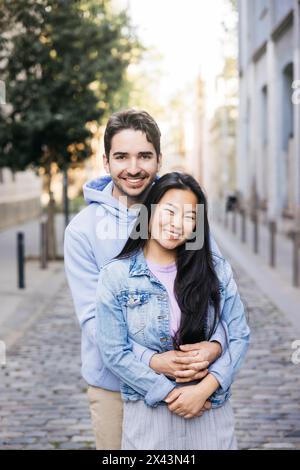 Cheerful man embracing his girlfriend from behind while standing outdoors. Couple enjoying themselves outdoors. Stock Photo