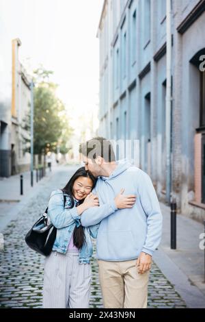 Interracial couple walking on a sidewalk holding hands. Young man and ...