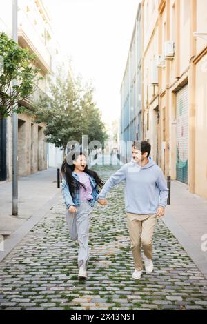 Interracial couple walking on a sidewalk holding hands. Young man and ...