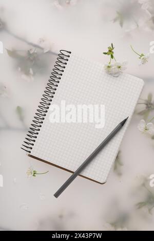Guest list. Notebook, pencil and beautiful cherry tree blossoms on spring floral background, flat lay Stock Photo