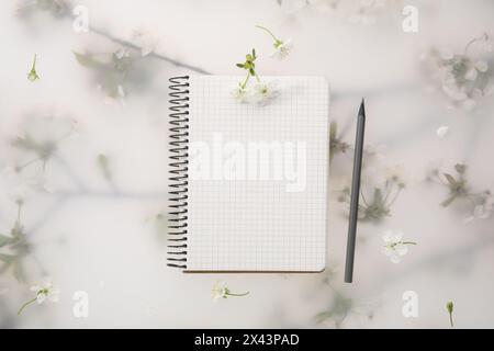 Guest list. Notebook, pencil and beautiful cherry tree blossoms on spring floral background, flat lay Stock Photo