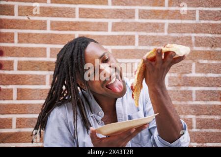 young man eating a slice of pizza in the street. Stock Photo