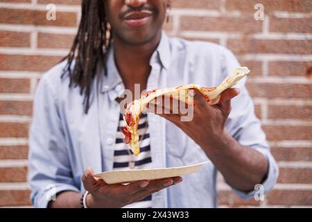 unrecognizable man holding a slice of pizza in his hand Stock Photo