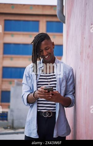 young caribbean man with braids on his head using his smart phone in the city Stock Photo