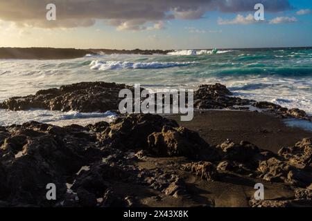 Black volcanic rocks on the Atlantic coast at sunset. Playa de las Malvas, Lanzarote, Canary Islands, Spain Stock Photo