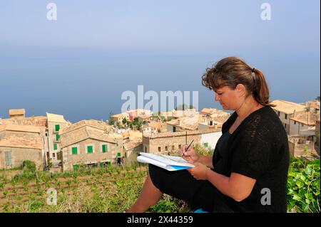 A woman sitting drawing in Banyalbufar, Mallorca. The Mediterranean sea in background Stock Photo