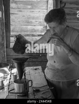 An infrared picture of a coffee farmers wife in the farmhouse smoking a cigar while brewing coffee over an open fire coffee, near Vinales, Cuba Stock Photo