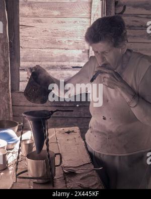 An infrared picture of a coffee farmers wife in the farmhouse smoking a cigar while brewing coffee over an open fire coffee, near Vinales, Cuba Stock Photo