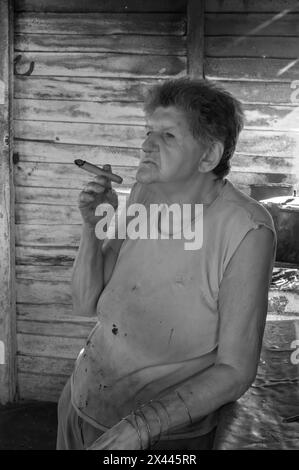 An infrared picture of a coffee farmers wife in the farmhouse smoking a cigar while brewing coffee over an open fire coffee, near Vinales, Cuba Stock Photo