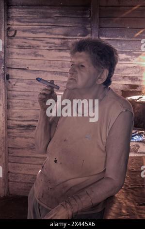 An infrared picture of a coffee farmers wife in the farmhouse smoking a cigar while brewing coffee over an open fire coffee, near Vinales, Cuba Stock Photo