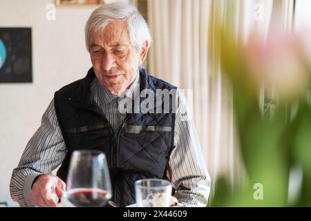 Elderly man sitting at table in restaurant and drinking red wine Stock Photo