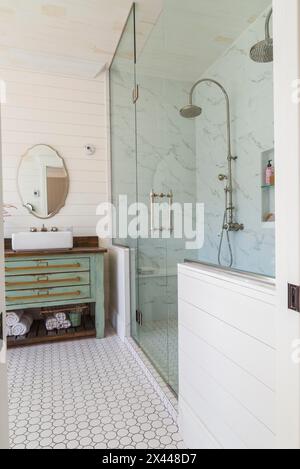 Green antique finish pine wood vanity with rustic wood plank countertop and white top-mounted vessel sink, glass and marble ceramic tile shower stall Stock Photo