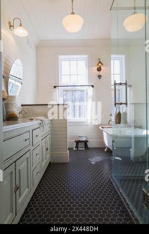 White antique style finish vanity with quartz countertop and two sunken sinks, freestanding claw foot bathtub, glass shower stall in kid's upstairs Stock Photo