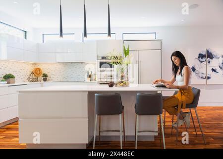 Interior designer Liza Castro in her kitchen with white high-gloss lacquered cabinets and island with grey leather bar stools and white quartz Stock Photo