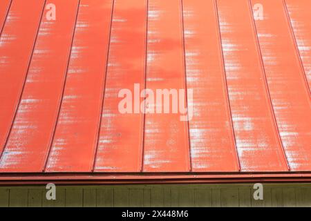 Weathered red standing seam sheet metal roof on old white vertical wood plank and red trim barn, Quebec, Canada Stock Photo