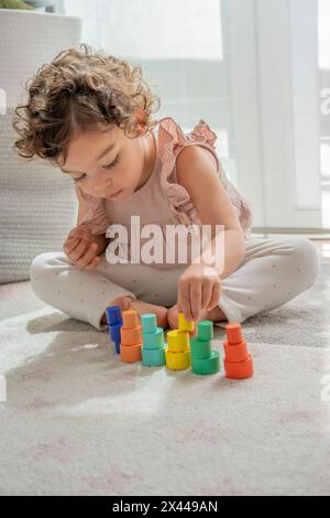 beautiful little girl dressed in pink plays concentratedly making towers and stacking blocks and colored wooden pieces. montessori material developmen Stock Photo