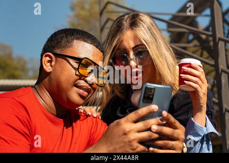 Happy interracial couple checking cell phone outdoors. Stock Photo