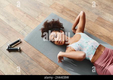 Curly African American woman in activewear laying on yoga mat for home workout. Stock Photo