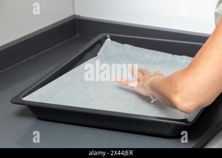 hand placing parchment paper on a dark tray, preparing for non-stick baking or cooking. Practical and essential step Stock Photo