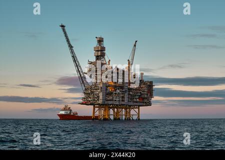 Offshore oil and gas jackup platform, during cargo operations with supply vessel in the sea and beautiful colourful sunset sky. Stock Photo