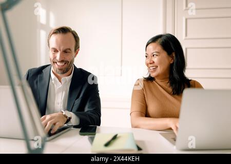 Smiling businesswoman looking at businessman using laptop in office Stock Photo