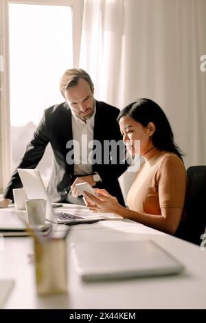 Businesswoman sharing smart phone with businessman in office Stock Photo