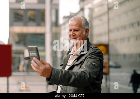 Smiling retired senior man using smart phone during video call Stock Photo
