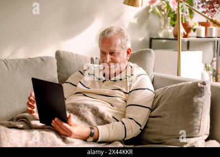 Retired senior man using digital tablet while sitting on sofa Stock Photo