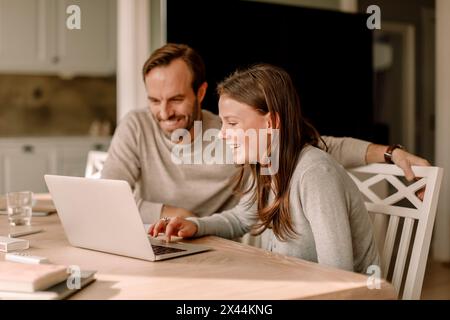 Mature man sitting by happy daughter using laptop for studying at home Stock Photo
