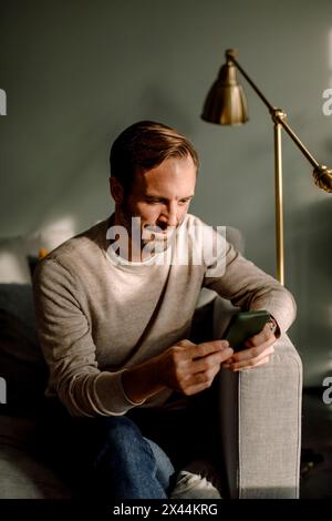 Mature man using smart phone while sitting on sofa at home Stock Photo