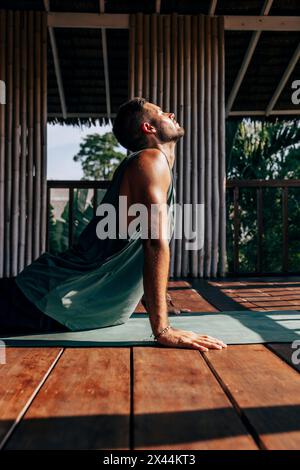 Side view of man doing Cobra pose on yoga mat over hardwood floor at wellness resort Stock Photo