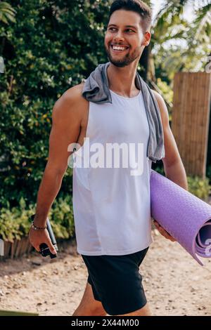 Smiling man holding yoga mat while walking at wellness resort Stock Photo