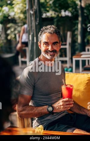Smiling mature man holding juice glass while sitting at wellness resort Stock Photo