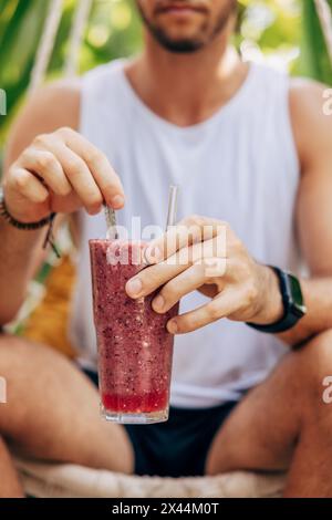 Midsection of man stirring berry smoothie while sitting at wellness resort Stock Photo