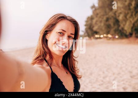 Portrait of smiling mature woman taking selfie at beach Stock Photo